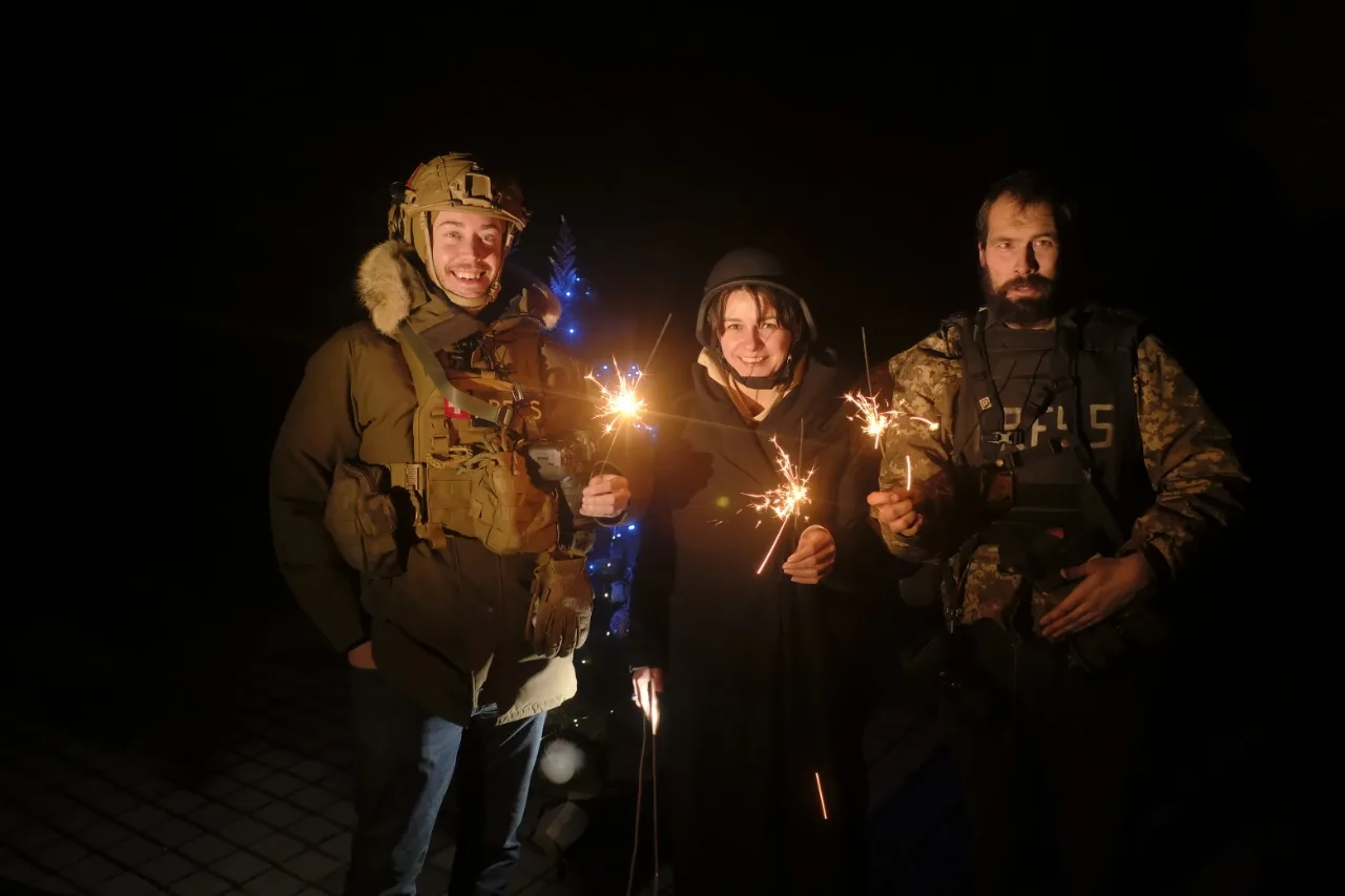 Three people in winter gear and body armour standing in the dark, each holding a lit sparkler.