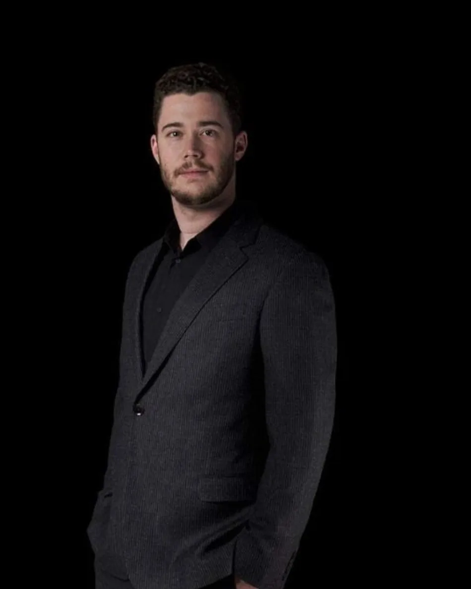 Stephan Goss, half length, in a dark suit against a black background.
