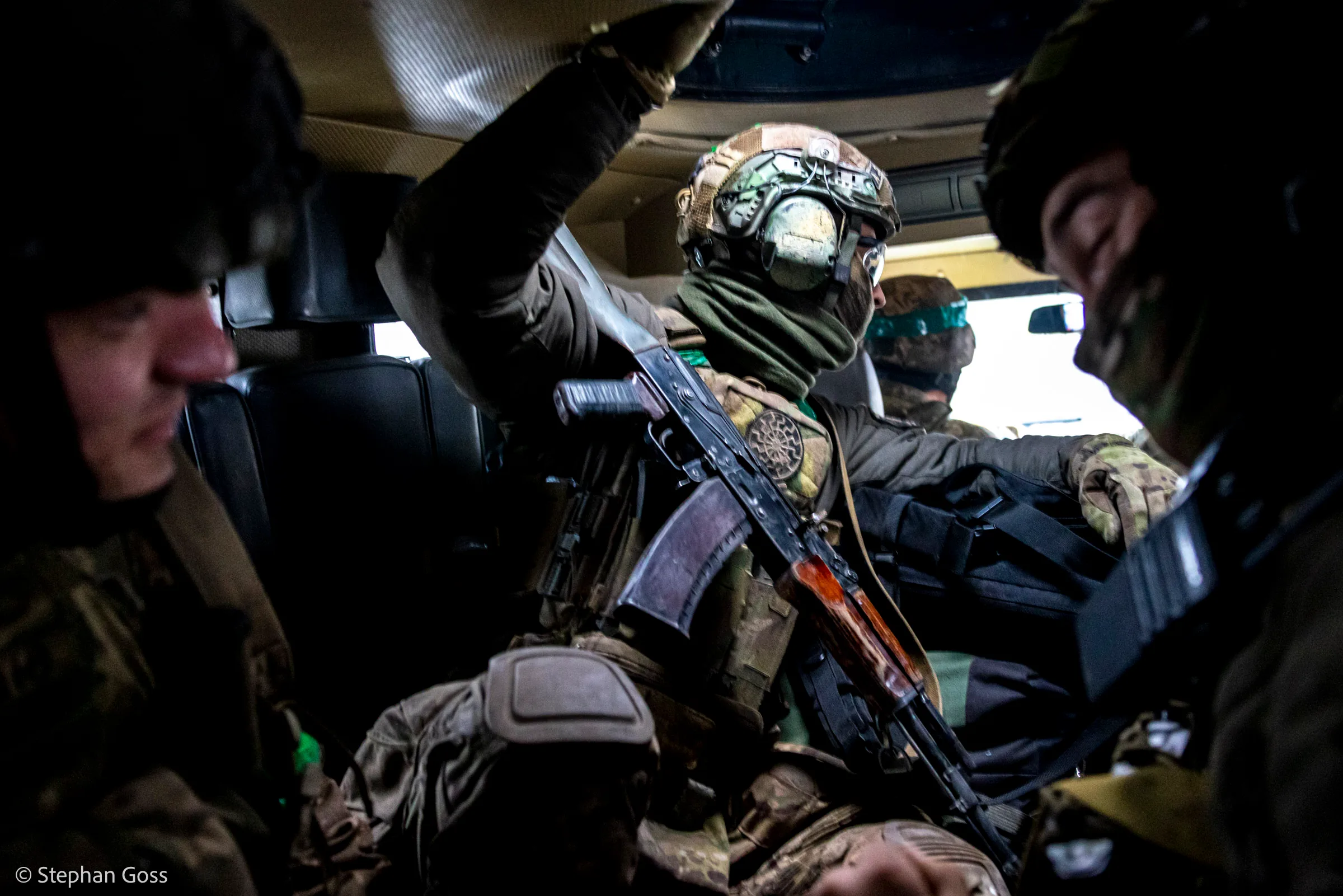 Ukrainian soldiers sit crowded in the dark interior of an armoured vehicle, rifles upright between their knees, one of them reaching for a handhold in the roof.